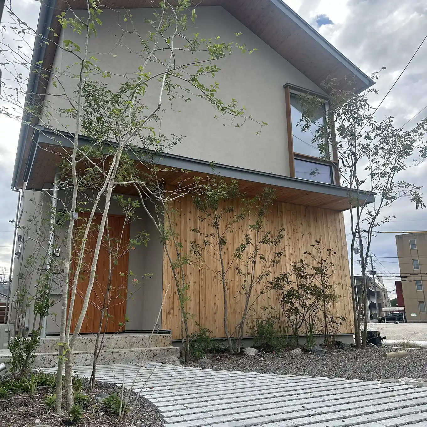 玄関まで続くアプローチとシンボルツリーのある住宅外観。植栽と敷石がバランスよく配置されている。