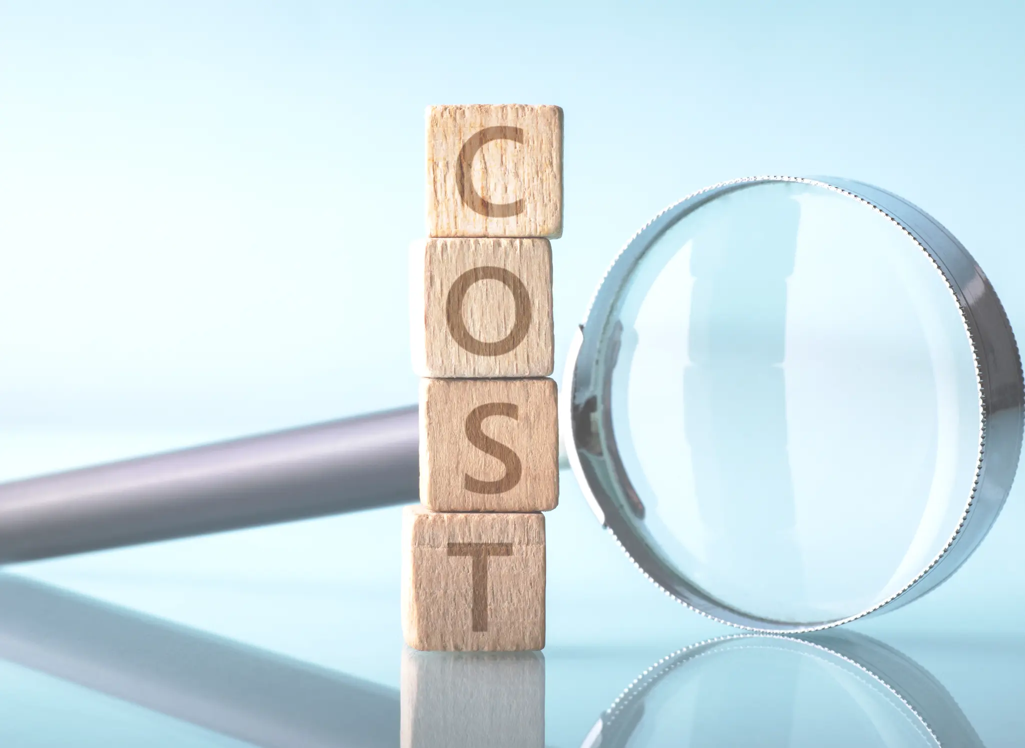 コスト削減を示すイメージ。COSTの文字が書かれた木製ブロックと虫眼鏡